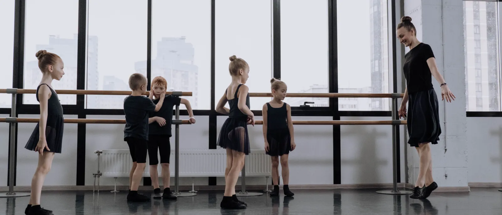 A ballet teacher and five young children at the barre in a bright studio