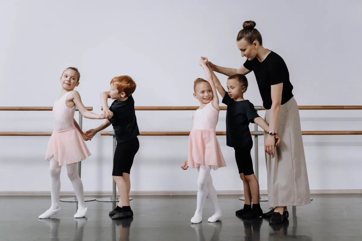 A ballet teacher guiding a young child's arms into position during a class